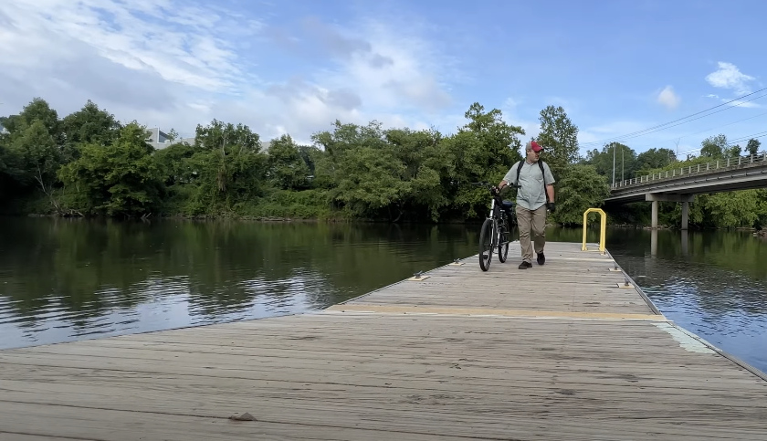 Person walking on a boardwalk while holding a bike by the lake
