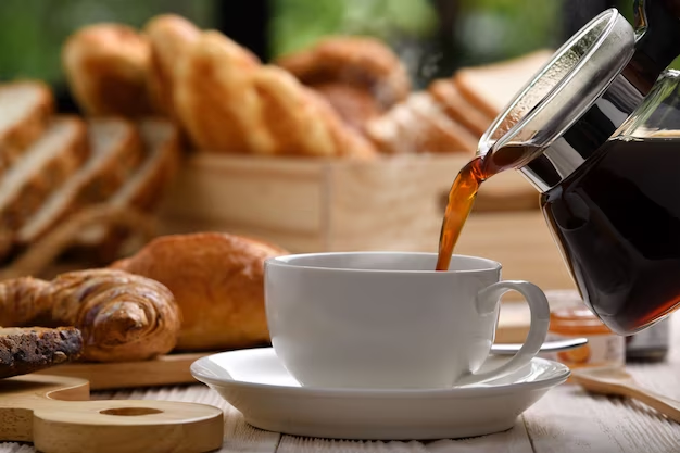 Pouring coffee into a mug with pastries beside it