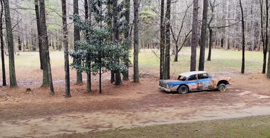 Image of a trail lined with tall trees and a very old, rotten car